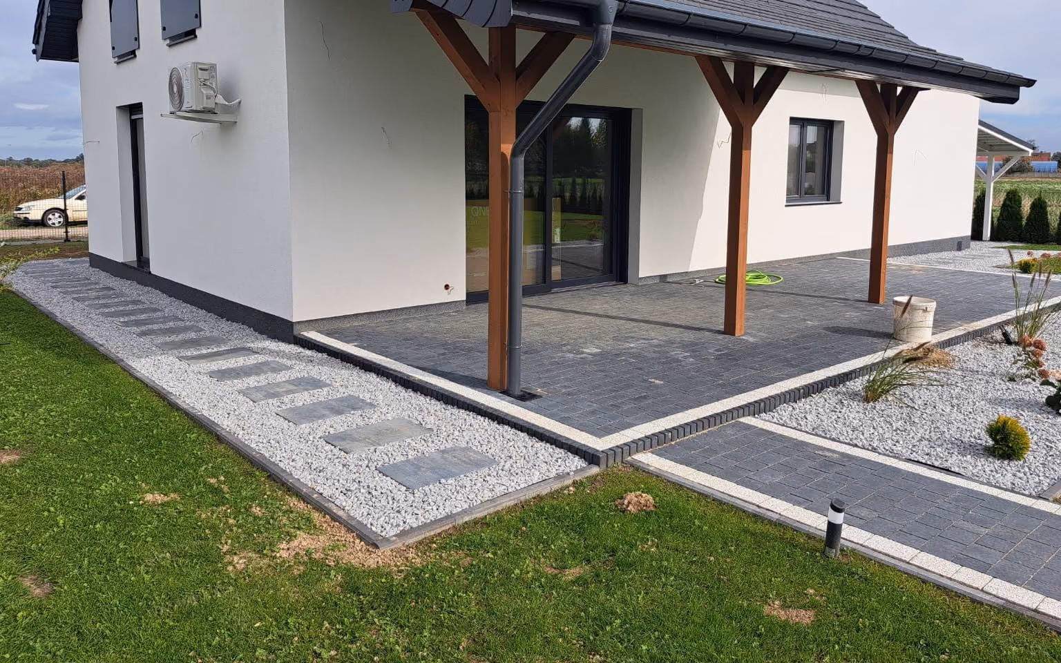 Opaska z ciemnej kostki wokół budynku, obok płyty ułożone w kruszywie